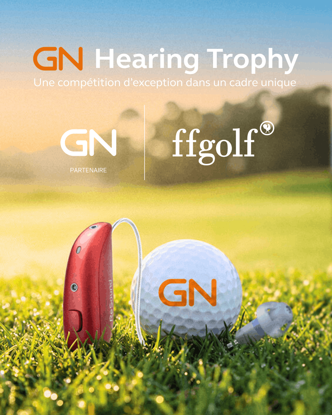Une aide auditive rouge posée sur l’herbe à côté d’une balle de golf blanche marquee du logo GN
