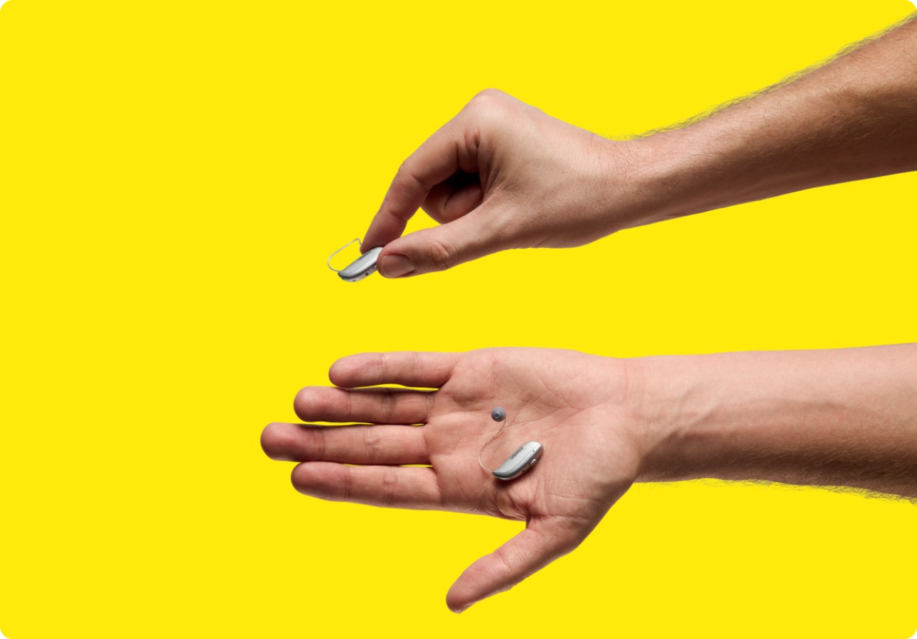 Two hands are holding hearing aids, showcasing their comfort and small size.