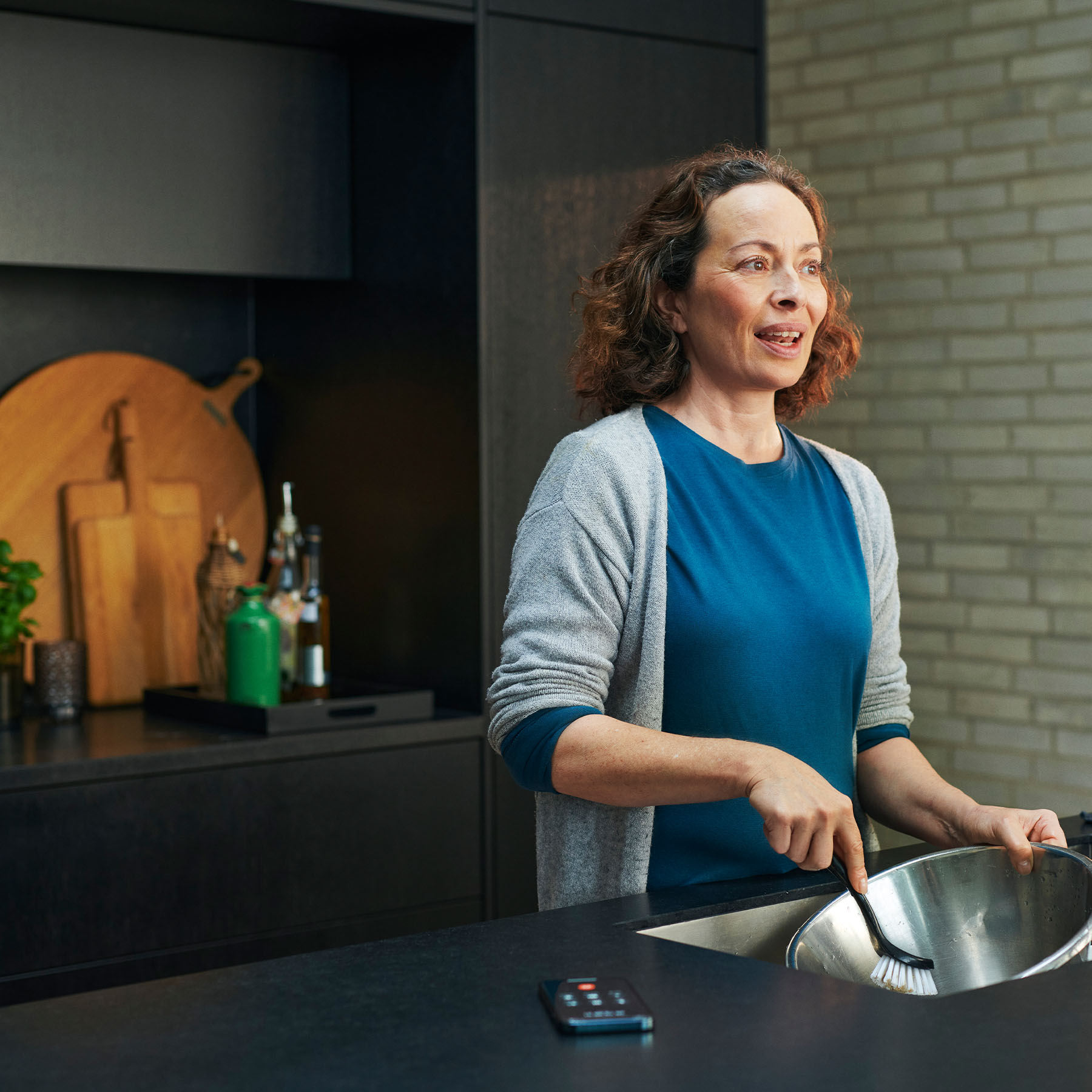 personne avec une aide auditive resound one lavant la vaisselle et parlant au téléphone